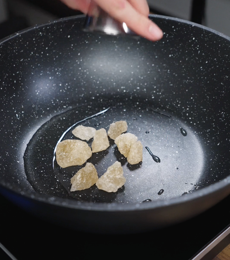 Golden rock sugar begins to melt and caramelize in a nonstick pan to form the flavor base of the braise.