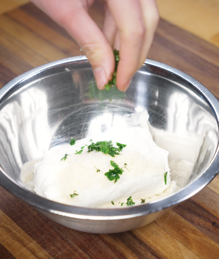 Parsley is added to a metal bowl of cream cheese, sugar, and parmesan to make the filling for Korean Garlic Cheese Bread.