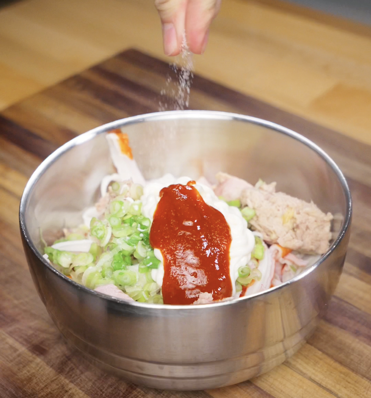 A bowl filled with crab, tuna, scallions, mayo, sriracha, and seasoning is being mixed to make the sushi bake topping.