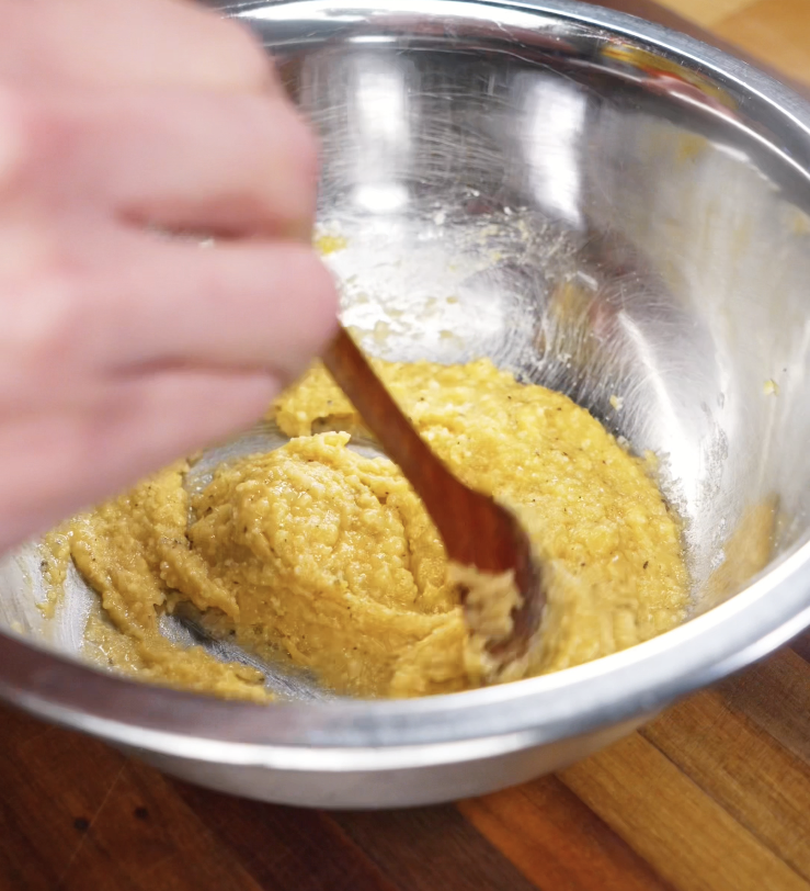 Egg yolks, miso paste, and grated parmesan are whisked together in a stainless steel bowl to form the creamy carbonara base.