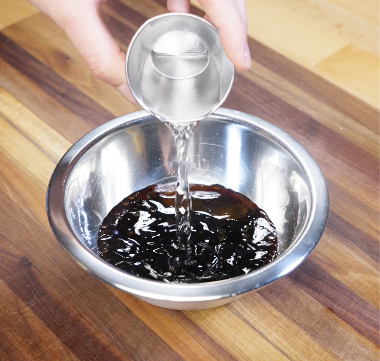 A shot of soy sauce, sesame oil, and shaoxing wine being poured into a bowl to make lo mein sauce.