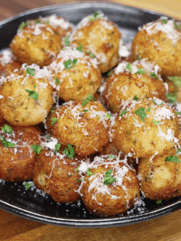 A black platter piled high with evenly crisped potato balls, garnished with grated parmesan and chopped parsley, ready to serve.