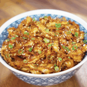 A serving of chili garlic butter noodles in a bowl, glistening with sauce and garnished with sesame seeds and scallions.