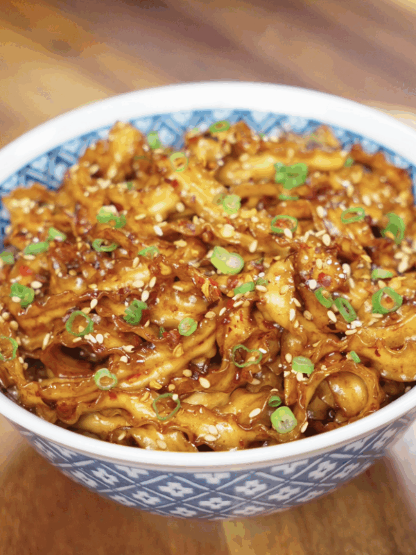 A serving of chili garlic butter noodles in a bowl, glistening with sauce and garnished with sesame seeds and scallions.