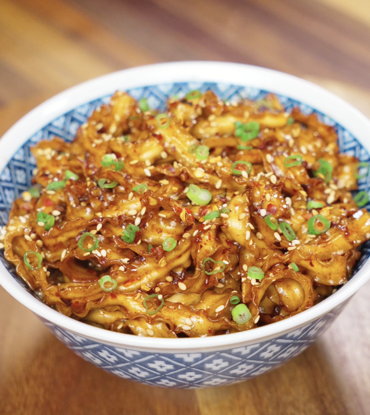 A serving of chili garlic butter noodles in a bowl, glistening with sauce and garnished with sesame seeds and scallions.