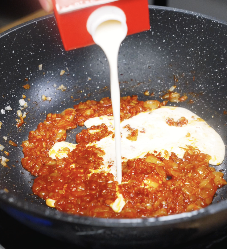 Heavy cream is poured into the pan with gochujang and onions to create a rich, spicy sauce.