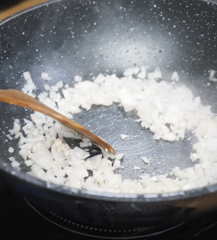 Finely diced onions are sautéed in rendered bacon fat in a nonstick pan until translucent and fragrant.