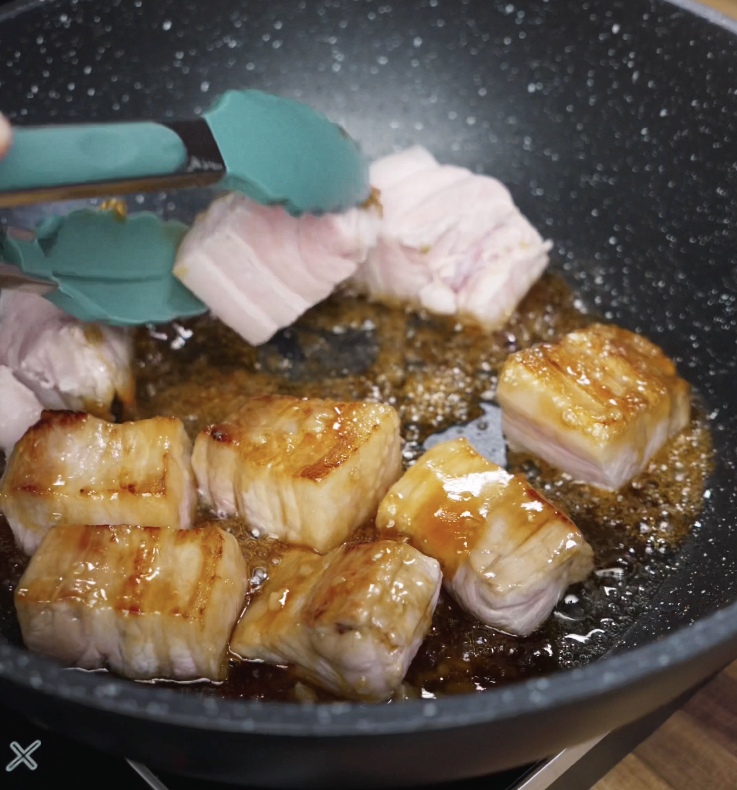 Par-cooked pork belly is added to the caramelized sugar, searing the meat and coating it in a glossy glaze.