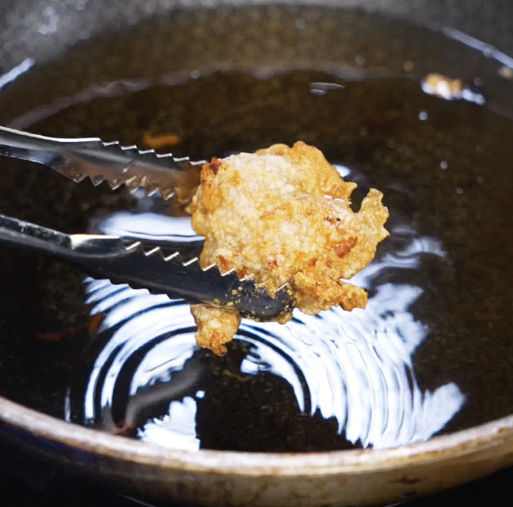 A golden-brown piece of chicken being lifted out of the oil after its second fry, showing extra crisp texture.
