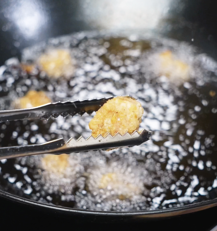 A golden, crispy piece of chicken being lifted from the oil during the second fry.