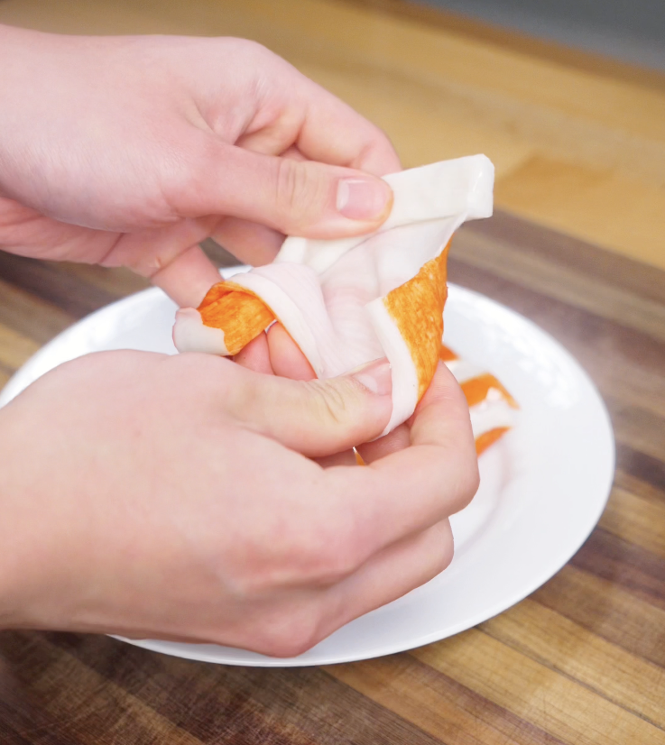 Hands pull apart imitation crab sticks into thin, shredded pieces for the creamy sushi bake topping.