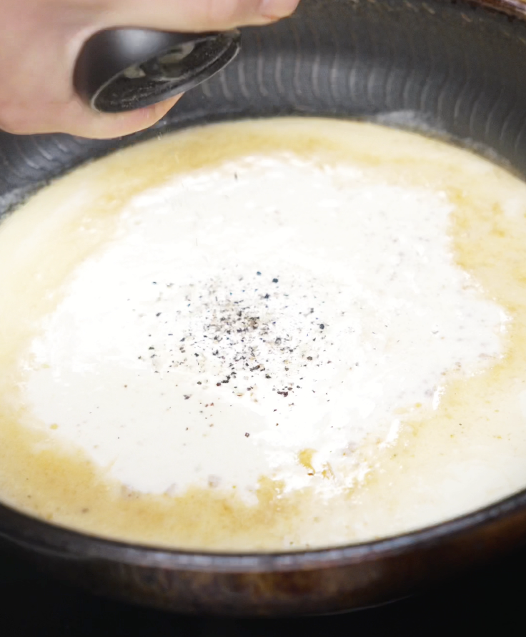 Cream, butter, and minced garlic simmer together in a pan with freshly cracked black pepper to start the Alfredo sauce.