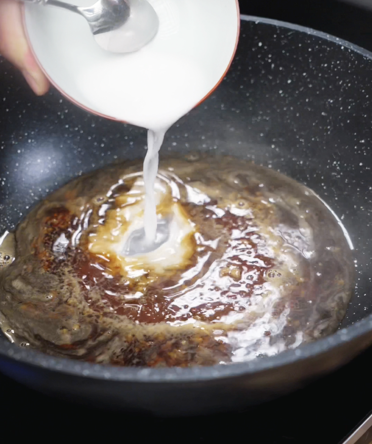 A cornstarch slurry is poured into a simmering pan of soy sauce, honey, garlic, and water to thicken the glaze.