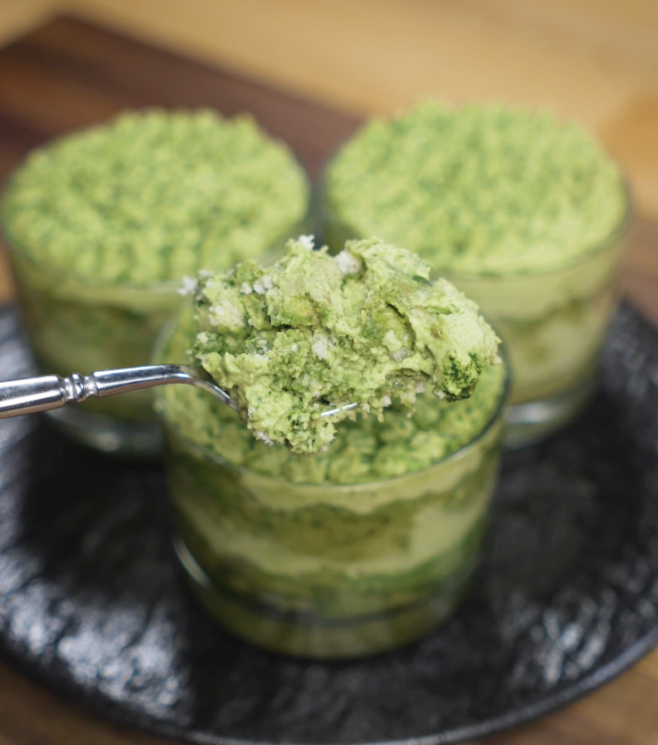 A close-up spoonful of matcha tiramisu reveals the creamy, fluffy texture of the layers inside.