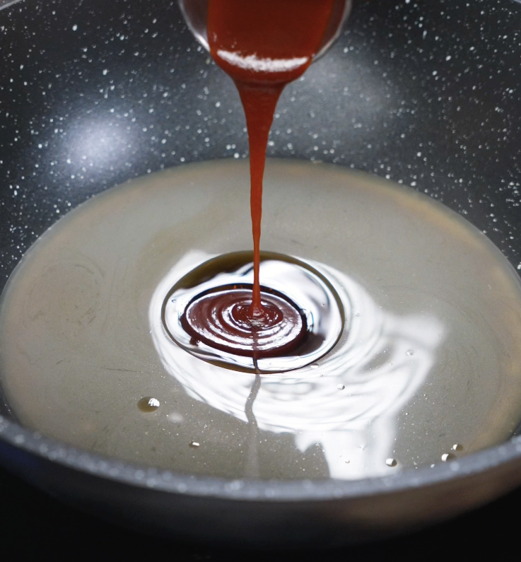 A thick soy-based General Tso’s sauce being poured into hot oil in a nonstick pan.