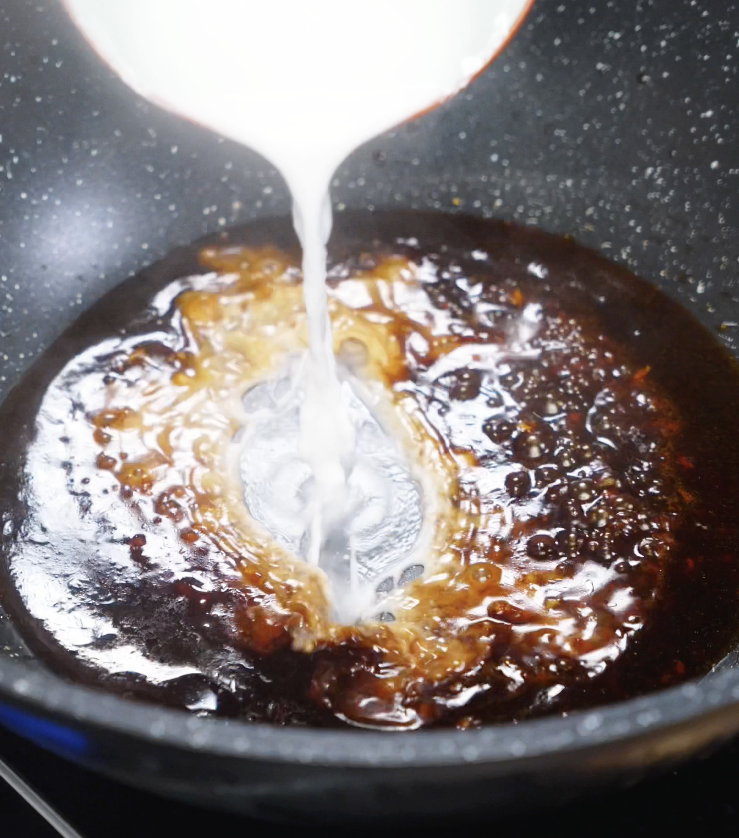 A cornstarch slurry is being poured into the simmering sauce to make it glossy and thick.