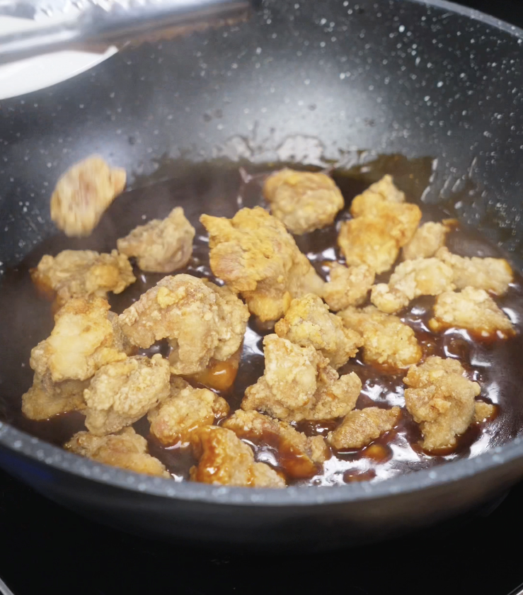 Crispy double-fried chicken being tossed in thick, glossy General Tso’s sauce in a pan.