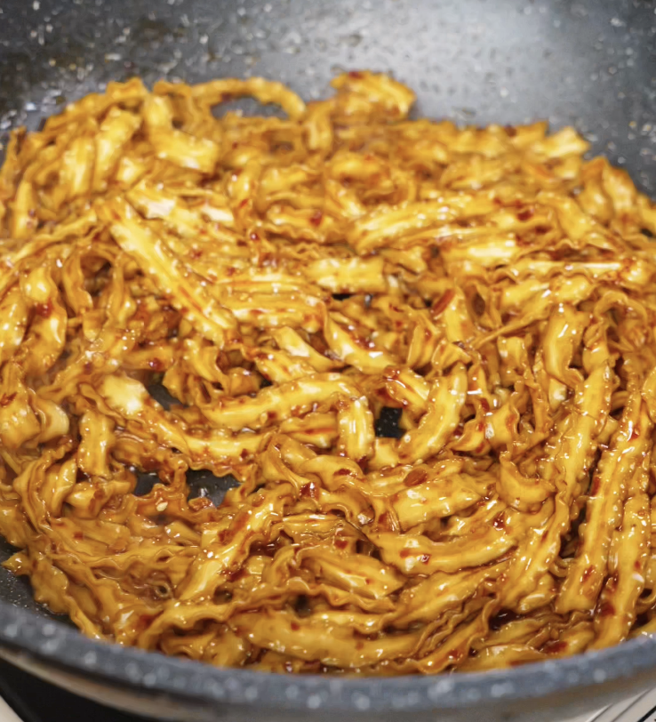 Cooked noodles being tossed into the pan, coated in the glossy, spicy chili garlic butter sauce.