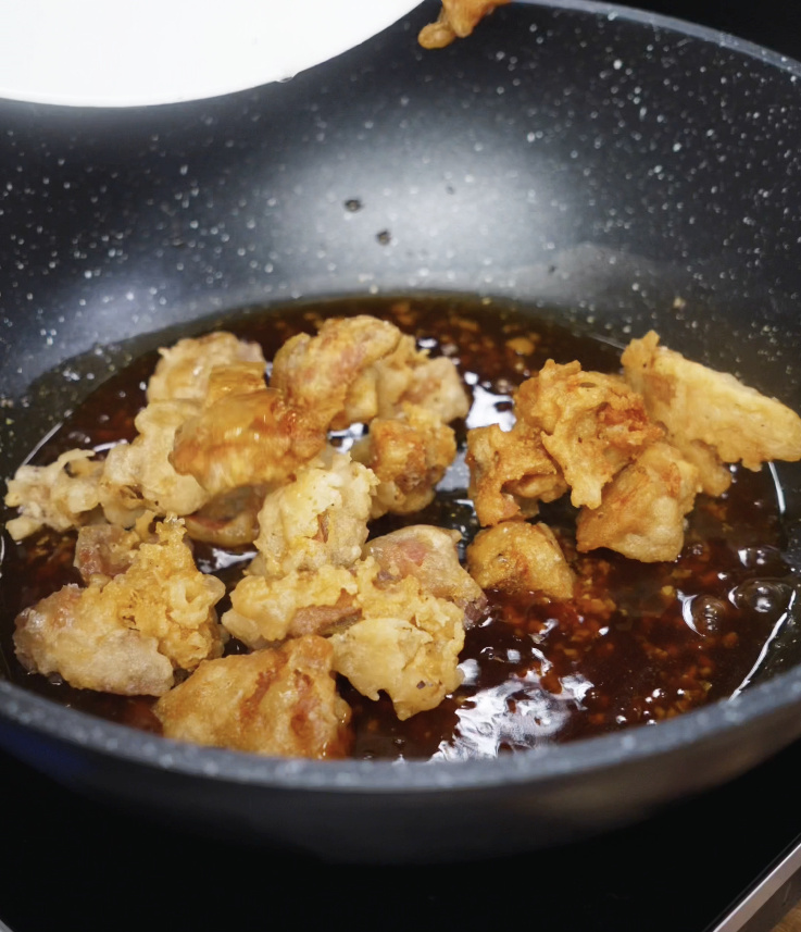 Double-fried chicken is added to the glossy soy garlic honey glaze in a pan, ready to be tossed and coated.