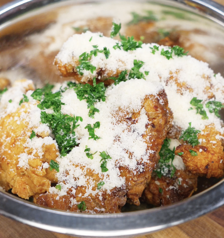 Freshly fried chicken tenders are placed in a bowl with parmesan and chopped parsley, ready to be tossed in buttery garlic goodness.