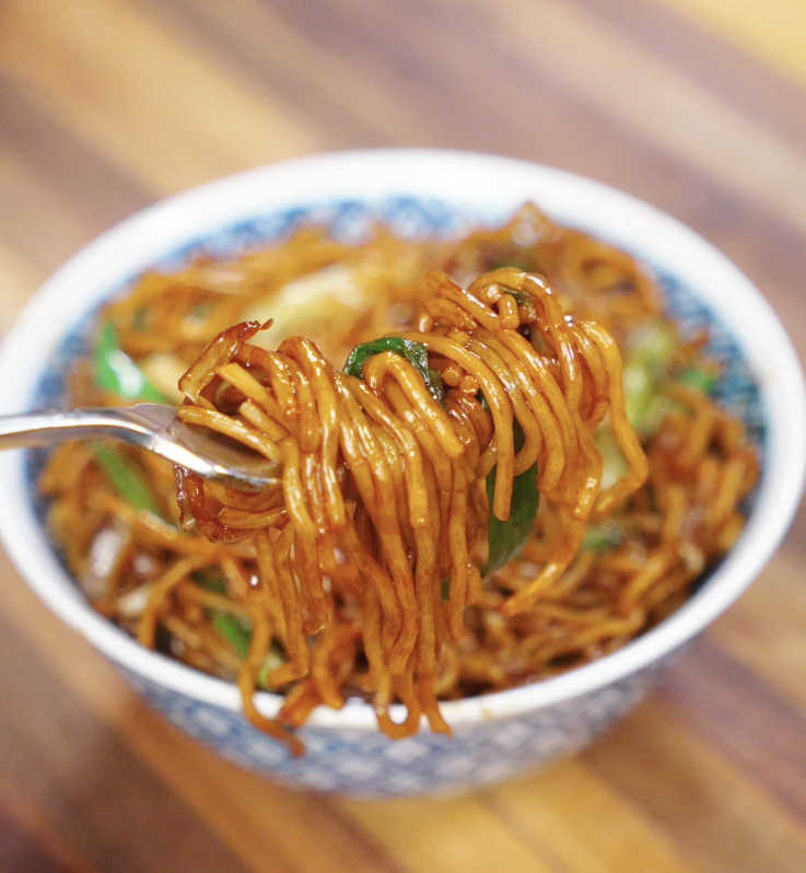 A close-up of chow mein noodles twirled around a fork, highlighting the savory sauce and glistening texture.
