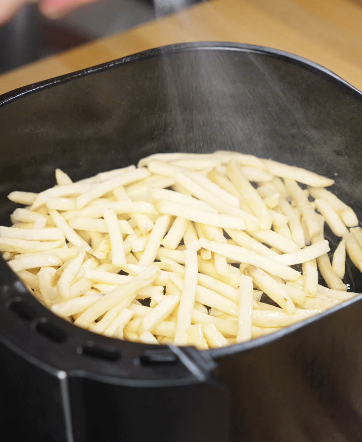 Frozen fries being seasoned as they cook in the air fryer basket, crisping up into golden, crunchy perfection.