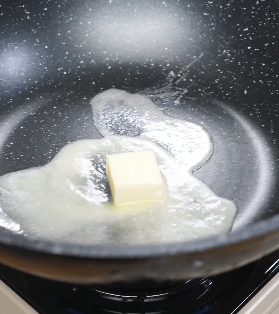 A slab of butter melting and foaming in a nonstick pan, turning golden brown and releasing a nutty aroma.