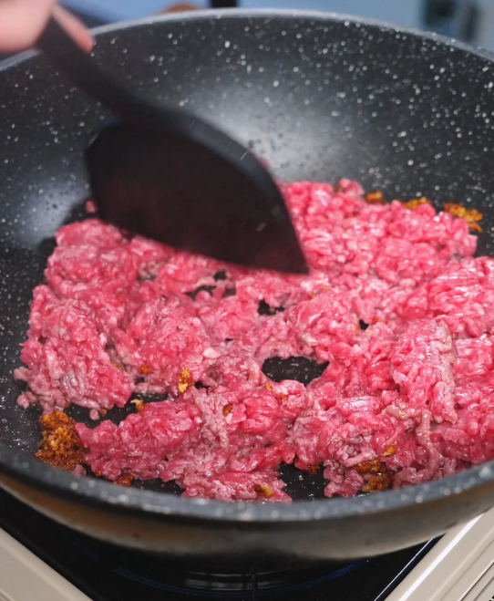 Ground beef being cooked in a hot pan and broken up with a spatula, beginning to brown as the base for Mongolian ground beef.