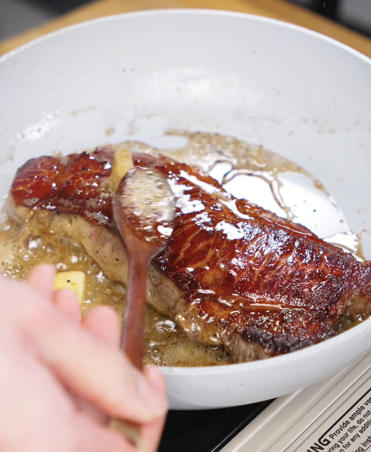 Melted butter bubbling around the steak while it’s spoon-basted in the pan, coating the meat in a glossy, savory layer for extra tenderness.