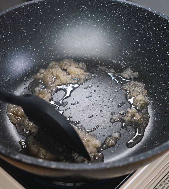Sugar slowly melting and caramelizing in oil in a pan, creating the deep amber base that gives red braised pork belly its signature color and sweetness.