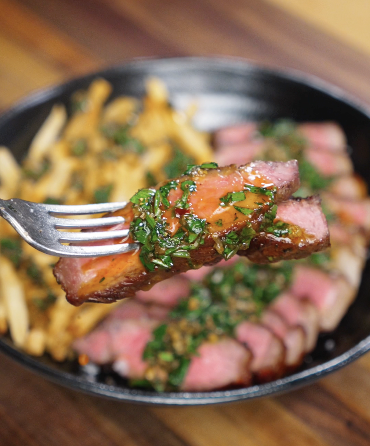 A fork lifting a juicy slice of medium-rare steak smothered in chimichurri, highlighting the glistening herbs and rich pink center.