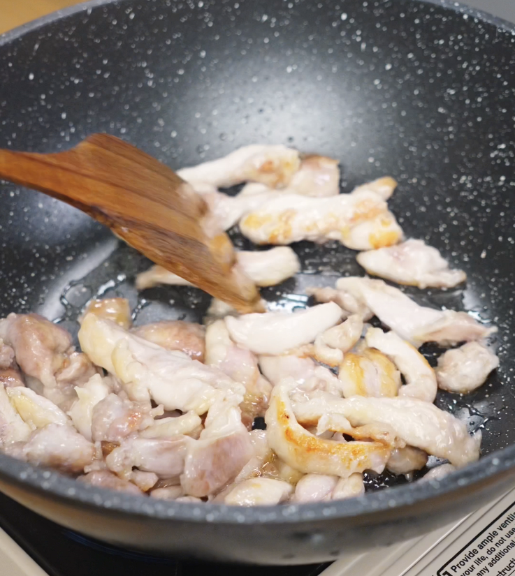 Sliced chicken thighs being stir-fried in a wok until golden brown and cooked through.