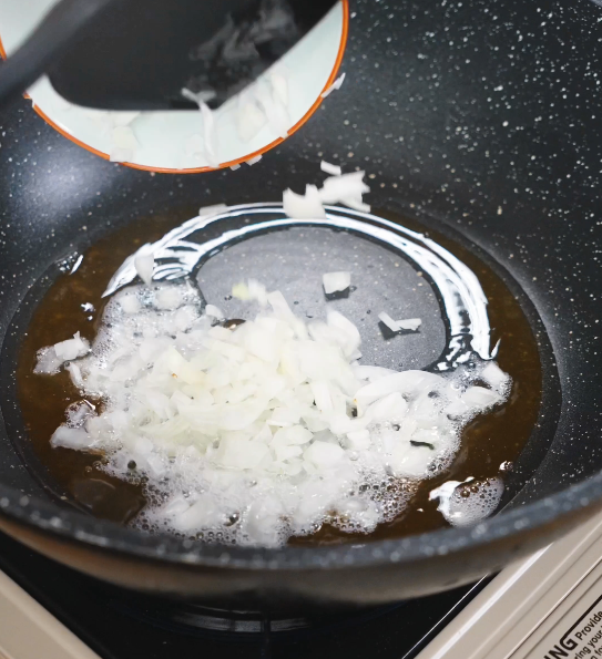 Chopped onions being added to caramelized sugar and oil, sizzling and turning translucent to build the aromatic foundation of the braising sauce.