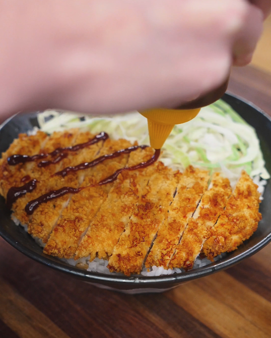 onkatsu sauce being drizzled over sliced air fryer chicken katsu served on rice with shredded cabbage, finishing the dish before serving.