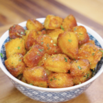 Golden brown garlic parmesan potatoes served in a patterned bowl, showcasing crispy texture and herb garnish for a cozy holiday side dish.