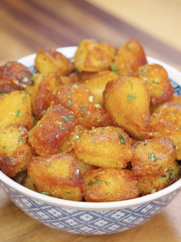 Golden brown garlic parmesan potatoes served in a patterned bowl, showcasing crispy texture and herb garnish for a cozy holiday side dish.