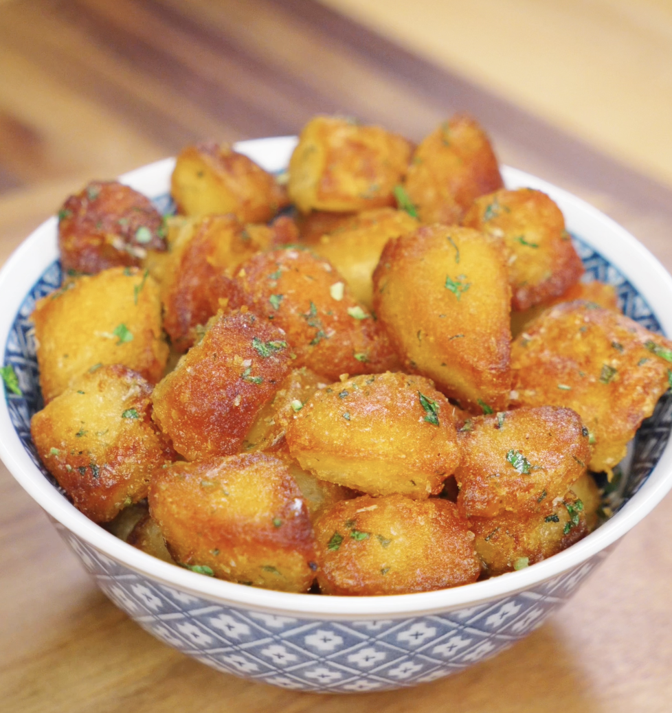 Golden brown garlic parmesan potatoes served in a patterned bowl, showcasing crispy texture and herb garnish for a cozy holiday side dish.