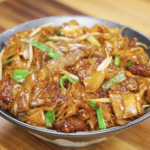 A full bowl of glossy beef chow fun with tender noodles, seared beef, scallions, and bean sprouts glistening under warm lighting.