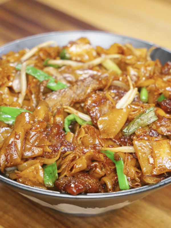 A full bowl of glossy beef chow fun with tender noodles, seared beef, scallions, and bean sprouts glistening under warm lighting.