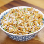 A blue patterned bowl filled with brown butter miso noodles, generously topped with parmesan and scallions, ready to serve.