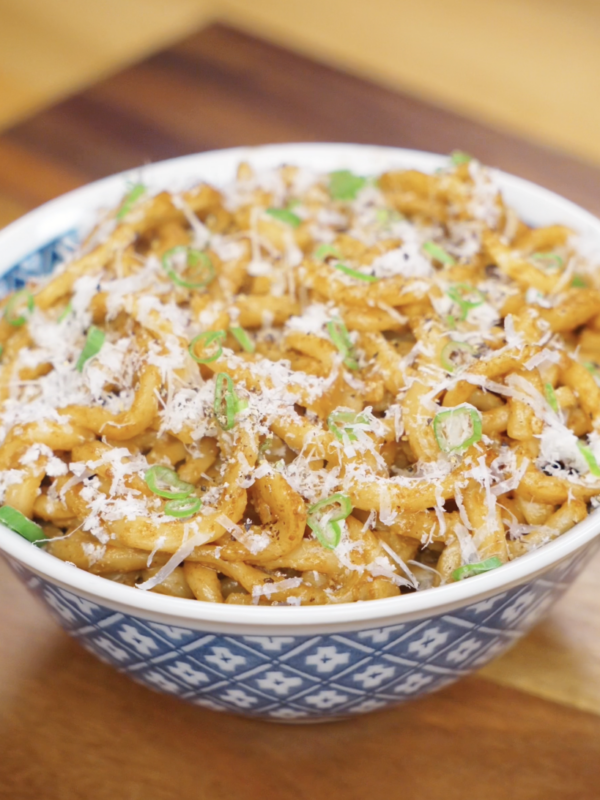 A blue patterned bowl filled with brown butter miso noodles, generously topped with parmesan and scallions, ready to serve.