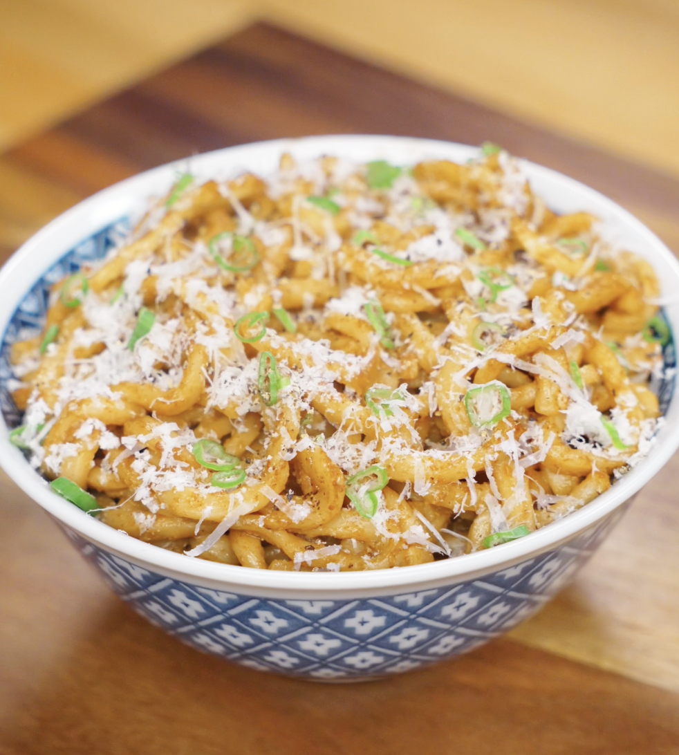 A blue patterned bowl filled with brown butter miso noodles, generously topped with parmesan and scallions, ready to serve.