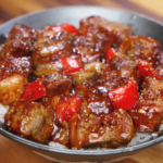 A bowl of black pepper beef served over rice with glossy sauce, tender beef cubes, and chunks of onion and bell pepper.