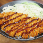 A bowl of air fryer chicken katsu sliced over steamed rice with shredded cabbage and tonkatsu sauce, showcasing a simple Asian dinner presentation.
