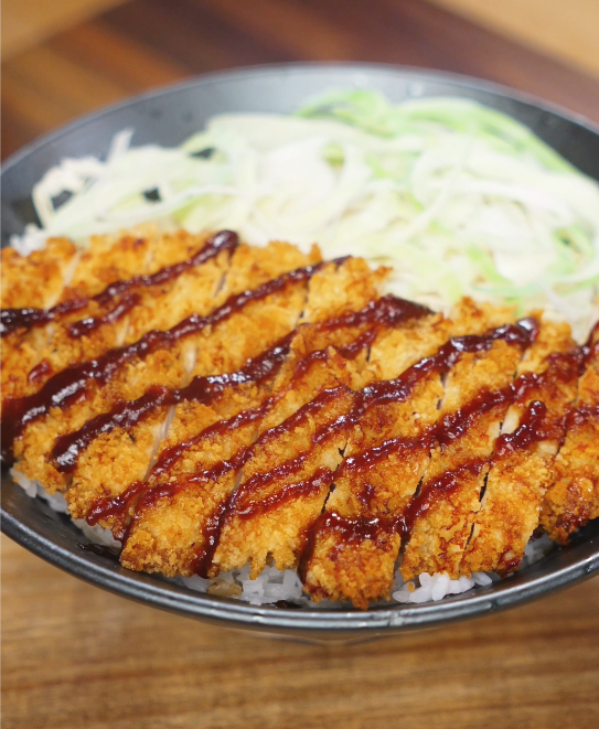 A bowl of air fryer chicken katsu sliced over steamed rice with shredded cabbage and tonkatsu sauce, showcasing a simple Asian dinner presentation.
