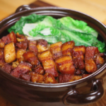 A finished bowl of red braised pork belly served over rice with optional steamed greens, showcasing the deep color, tender texture, and cozy presentation.