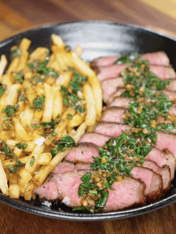 A cozy plate of steak frites with crispy golden fries and perfectly pink sliced steak, topped with fresh chimichurri for a vibrant, herb-packed finish.