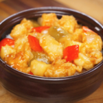A bowl of sweet and sour chicken coated in a glossy pineapple-studded sauce with chunks of onion and bell peppers, showcasing the classic takeout-style finish.