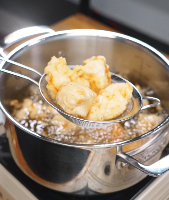 Lightly battered chicken pieces frying in hot oil until pale golden and crisp, being lifted from the oil with a strainer.