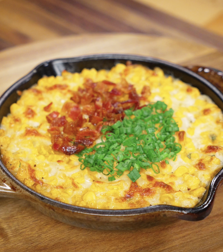 Finished Korean corn cheese topped with crispy bacon bits and scallion greens, ready to serve in a cast iron dish.